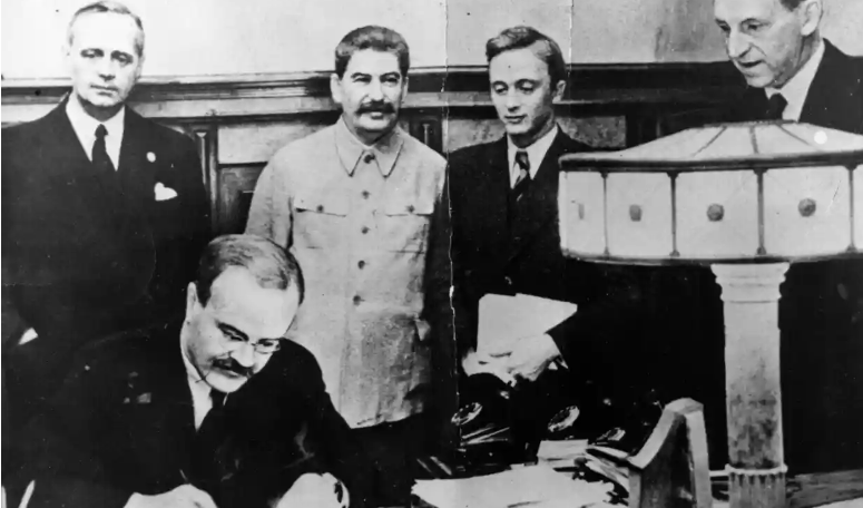 Vyacheslav Molotov, Russian foreign minister, signs the non-aggression pact negotiated between Soviet Russia and Germany, at the Kremlin, Moscow. Standing behind him is his German counterpart Joachim von Ribbentrop (left), and Joseph Stalin (centre), 23 August 1939. Photograph: Keystone/Getty Images
